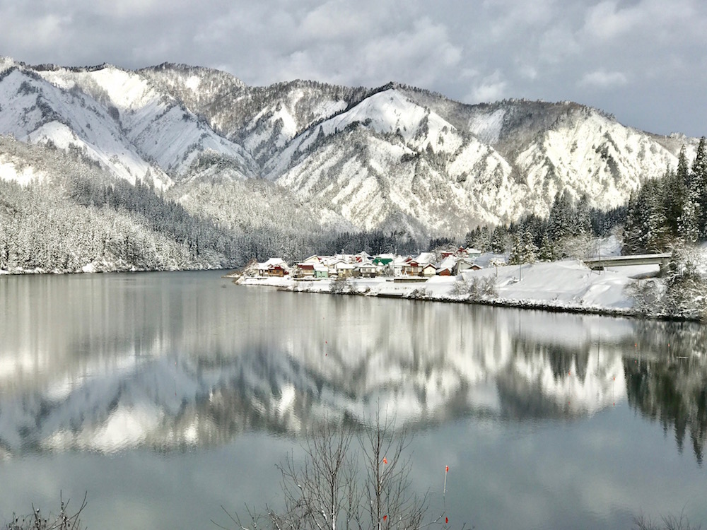 雪の大志集落のある只見川に雪山が映る